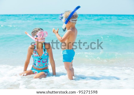 Smiling Happy brother and sister posing on a beach wearing snorkeling equipment. In the background the sea
