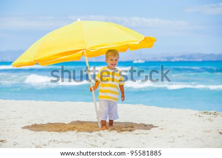 Cute 2 years old boy with big umbrella on tropical beach