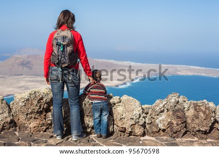 Back view young mother with backpack and son standing on cliff\'s edge and looking to a island.