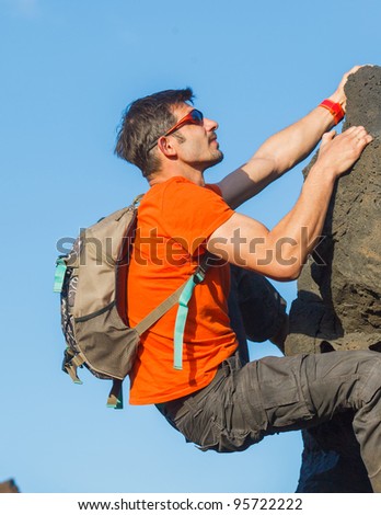 Young man in glasses with backpack climbing outdoor wall.