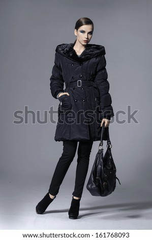 Full body young elegant woman in coat with holding bag posing