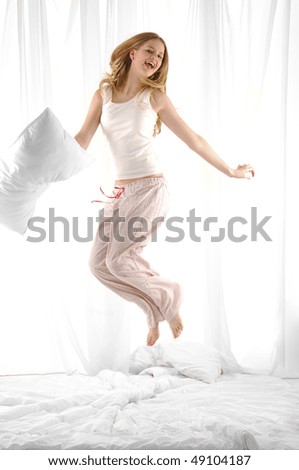 blond woman holding pillow jumping on her bed