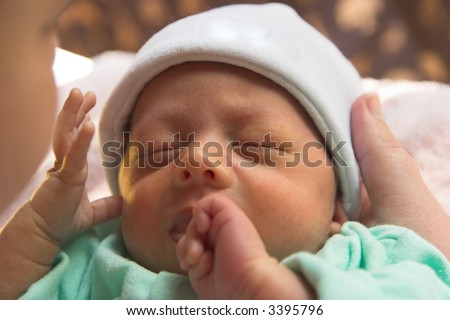 Mother holding sleeping baby with baby biting hand
