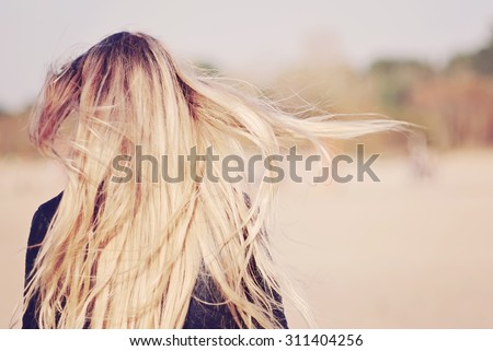 Back view of the young female with beautiful blond straight long hairs in motion