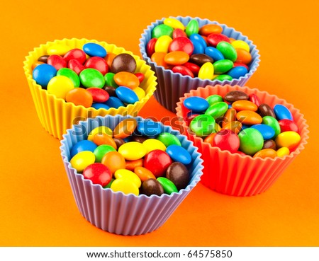 Bright colred sweets in cup cake holders on an orange background