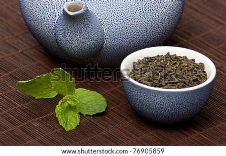 A chinese teapot and cup with fresh green mint