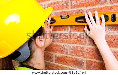A young female in a hard hat checking if brick wall is level