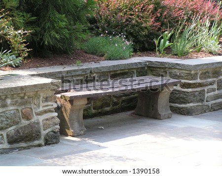 wood and concrete bench set in a niche along a stone retaining wall with garden behind