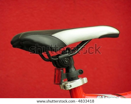 Black and white leather bicycle seat in front of a vivid red exterior wall.