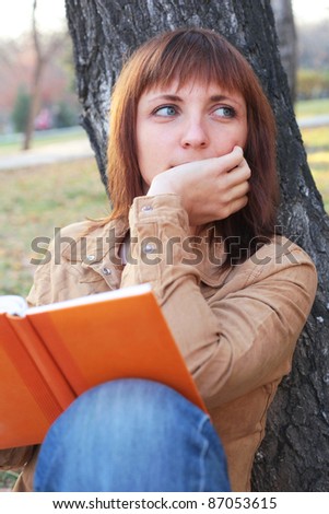 closeup image of the pretty young girl reading a book and dreaming in the park