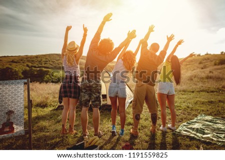 Happy young friends enjoy a sunny day in nature. They\'re looking at sun and greeting,  happy to be together.