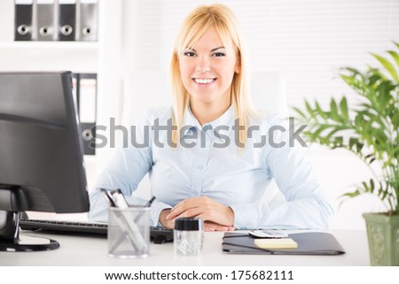 Businesswoman in the office. Sitting at the table with computer and Looking at camera.