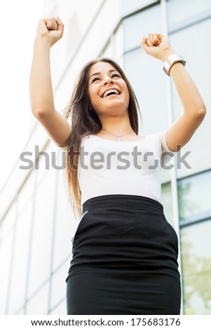 Successful Businesswoman standing on the street in front of Office Building with Arms Raised.
