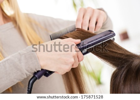 Hairdresser straightening long brown hair with hair irons.