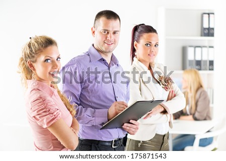 Three smiling co-workers standing in the office with crossed arm and looking at the camera.