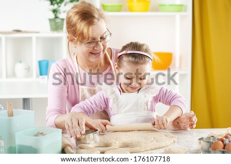 Beautiful happy grandmother learning her granddaughter to Baking in the kitchen.