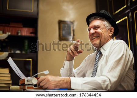 Retro Senior man, journalist, writer, writing on traditional Typewriter. He is sitting with a cigarette in his hand and smiling.