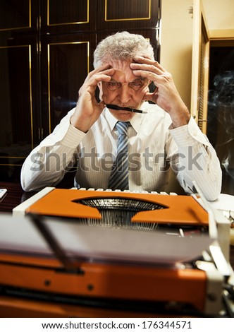 Retro Senior man, journalist, writer, sitting with a traditional Typewriter and thinking, with pen in a mouth.