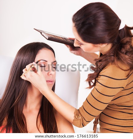 Female makeup artist darkening eyebrows with eyebrow pencil on Young Attractive woman.