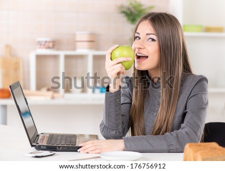 Businesswoman in the kitchen eating apple and reading mail on laptop before going to work.