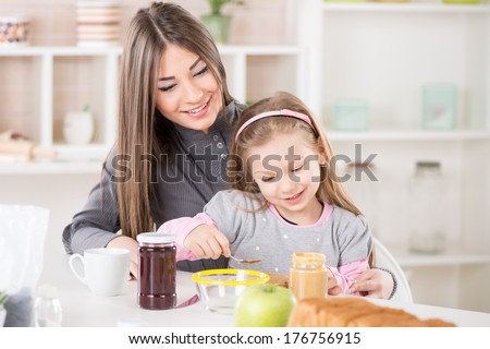 Cute little girl sitting in the mother lap and smearing peanut butter on bread.