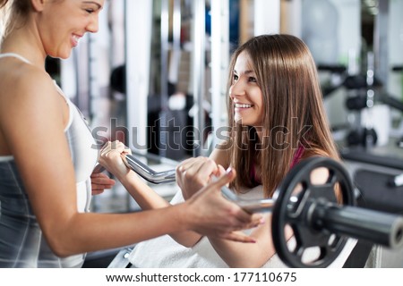 Cute Sporty young woman doing exercise in a fitness center with her personal coach. She is working exercises to strengthen her bicep.
