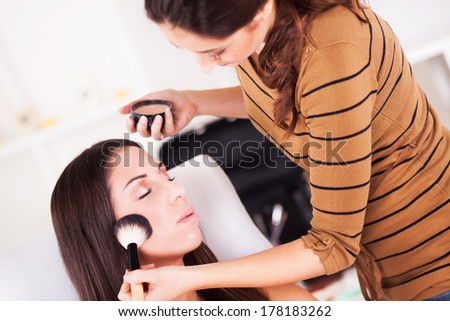 Female makeup artist applying blush on cheeks Young Attractive woman.