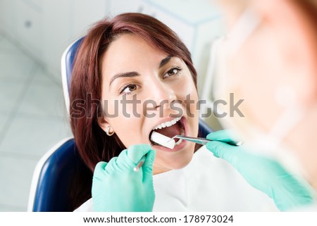 Female dentist preparing patient for dental treatment. She is inserting cotton pad in patient mouth. Selective focus, focus on the patient.