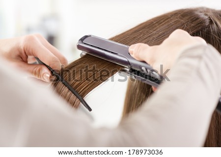 Hairdresser straightening long brown hair with hair irons.