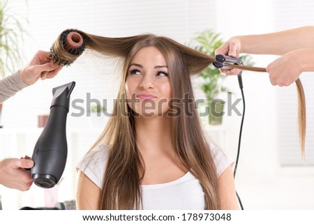 Hairdressers straightening long brown hair with hair dryer and round brush and hair irons.