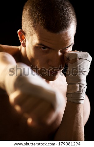 Young Fighter on black background in attack position. Only Boxing Straps on his hands.