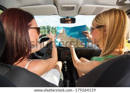 Young women with a tourist map looking for directions. They sitting in the car and going on holiday.
