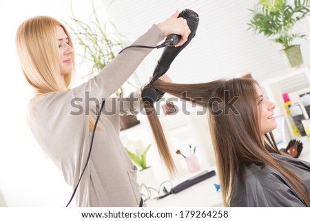 Hairdresser drying long brown hair with hair dryer and round brush.