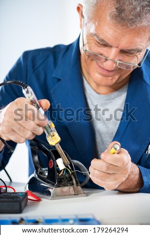 Senior adult Electrician repairing old iron with soldering iron.