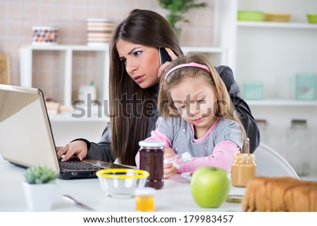 Overworked Business Woman and her little daughter in the morning. Mother read mail and make phone calls before going to work. Daughter salt breakfast.