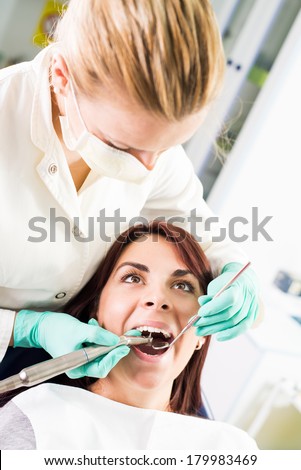 Female dentist with dental drill repairing tooth on the female patient in the office. Selective focus, focus on the patient.