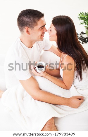 Romantic young couple drinking coffee in bed and touching noses.