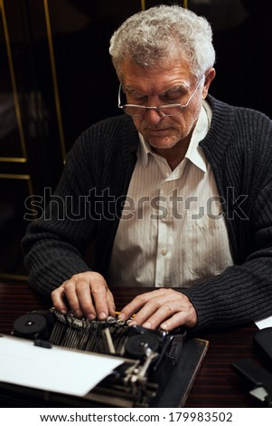 Retro Senior man writer with glasses writing on Obsolete Typewriter.