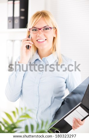 Busy Beautiful Businesswoman with glasses use mobile phone in the office and holding documents.