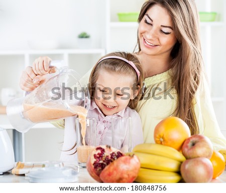 Beautiful young woman and cute little girl pouring juice from blender in the glass. In the kitchen concept.