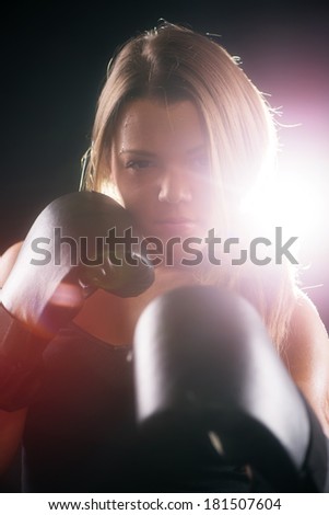 Portrait of Young beautiful boxing girl standing with a guard ready to punch. Black background with light effects and lens flare.