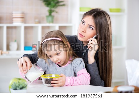 Overworked Business Woman and her little daughter in the morning. Overworked mother make phone calls before going to work. Preparing cereal with milk for her daughter and spilling milk next to bowl.
