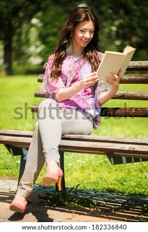 Young Beautiful Woman Reading Book In The Park, and sitting on the Park Bench.