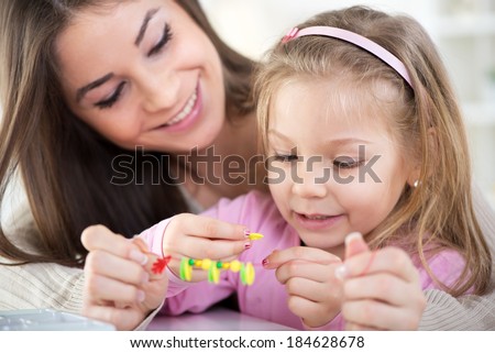 Mother and daughter playing at home. They Making bead bracelets.