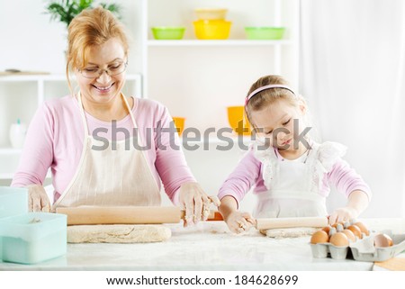 Beautiful happy grandmother and granddaughter a rolling pin together in the Kitchen.