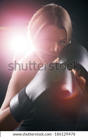 Portrait of Young beautiful boxing girl standing with a guard ready to punch. Black background with direct light with lens flare.