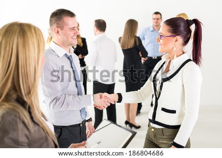 Successful business people shaking hands at the meeting because of Successful Agreement with coworkers standing in background.