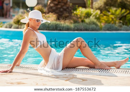 Young beautiful woman enjoying the sun and sitting on edge of the pool.