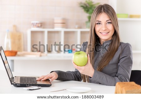 Businesswoman in the kitchen with apple reading mail on laptop before going to work.