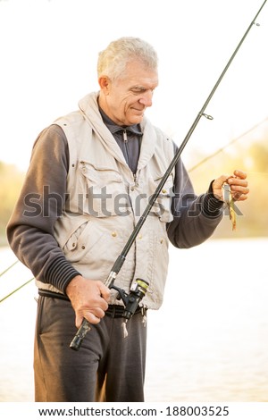Senior Fisherman holding fishing rod with fish on the hook.